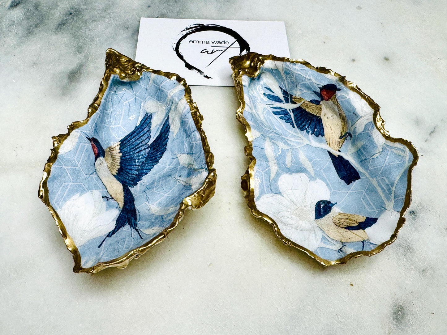 Handmade Dorset oyster shell trinket dish featuring elegant blue bird design with hand gilded gold leaf edging and glossy crystal clear resin finish, luxury coastal jewellery holder and decorative ring dish inspired by birds of paradise and coastal nature