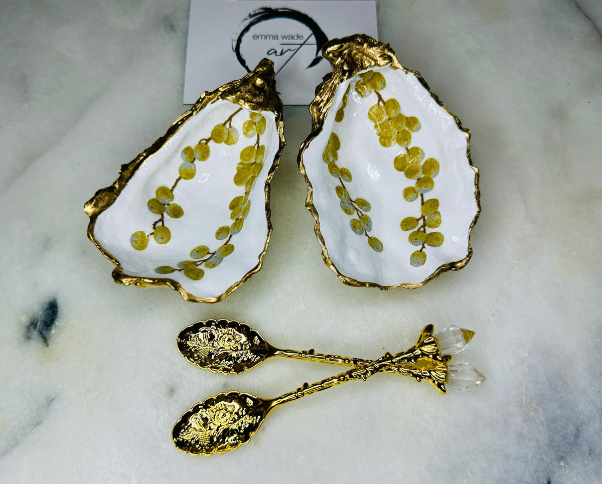 Pair of white and gold oyster shell salt and pepper pinch pots with delicate berry botanical design, hand gilded gold leaf edging and glossy resin finish. Handmade Dorset coastal shell dishes styled with gold crystal spoons on a marble background.
