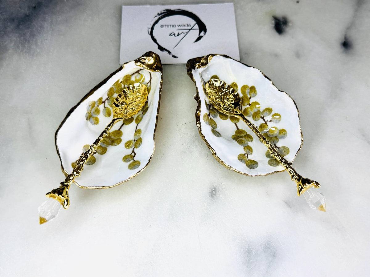 Pair of white and gold oyster shell salt and pepper pinch pots with delicate berry botanical design, hand gilded gold leaf edging and glossy resin finish. Handmade Dorset coastal shell dishes styled with gold crystal spoons on a marble background.