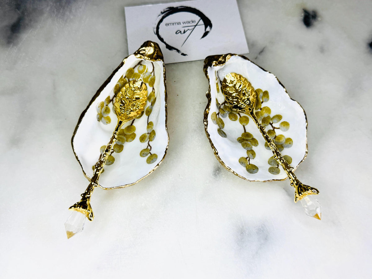 Pair of white and gold oyster shell salt and pepper pinch pots with delicate berry botanical design, hand gilded gold leaf edging and glossy resin finish. Handmade Dorset coastal shell dishes styled with gold crystal spoons on a marble background.