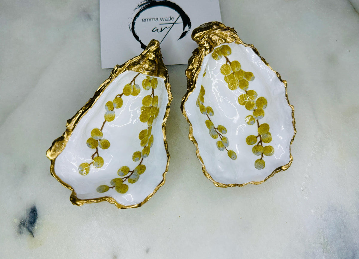 Pair of white and gold oyster shell salt and pepper pinch pots with delicate berry botanical design, hand gilded gold leaf edging and glossy resin finish. Handmade Dorset coastal shell dishes styled with gold crystal spoons on a marble background.