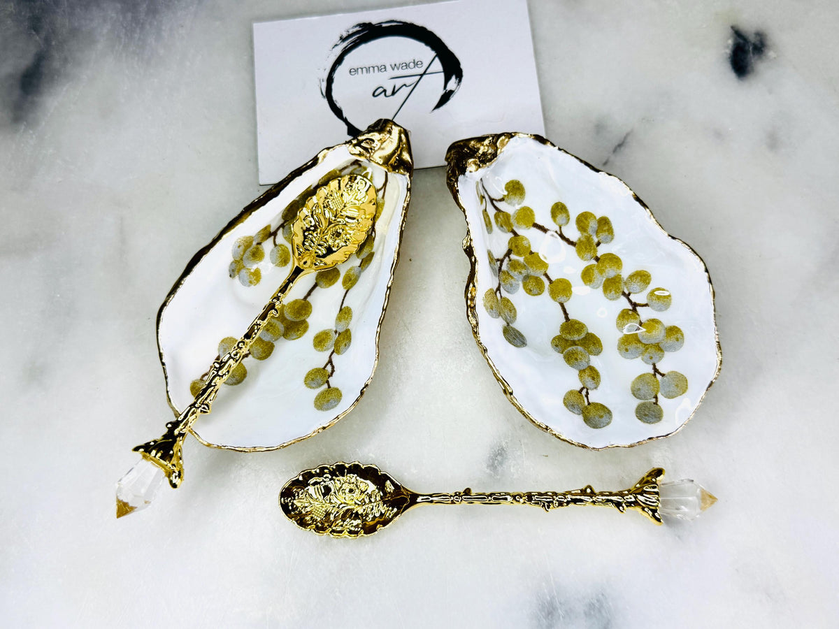 Pair of white and gold oyster shell salt and pepper pinch pots with delicate berry botanical design, hand gilded gold leaf edging and glossy resin finish. Handmade Dorset coastal shell dishes styled with gold crystal spoons on a marble background.