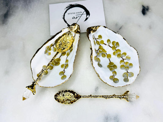 Pair of white and gold oyster shell salt and pepper pinch pots with delicate berry botanical design, hand gilded gold leaf edging and glossy resin finish. Handmade Dorset coastal shell dishes styled with gold crystal spoons on a marble background.