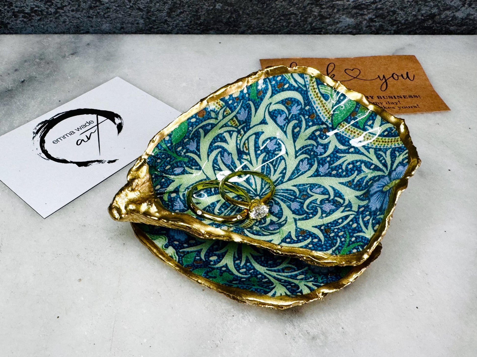 Luxury Dorset oyster shell ring and jewellery box with matching lid, finished with gold leaf detailing and glossy resin. 4 designs avaialble including natural oyster shell with gold rim and pearl interior, gold leaf shell with natural white interior, or gold leaf shell with decoupage interior. Shown holding rings on a light background, highlighting the natural shell shape and polished handcrafted coastal keepsake style. Ideal as an engagement ring box, wedding ring holder, or jewellery keepsake.