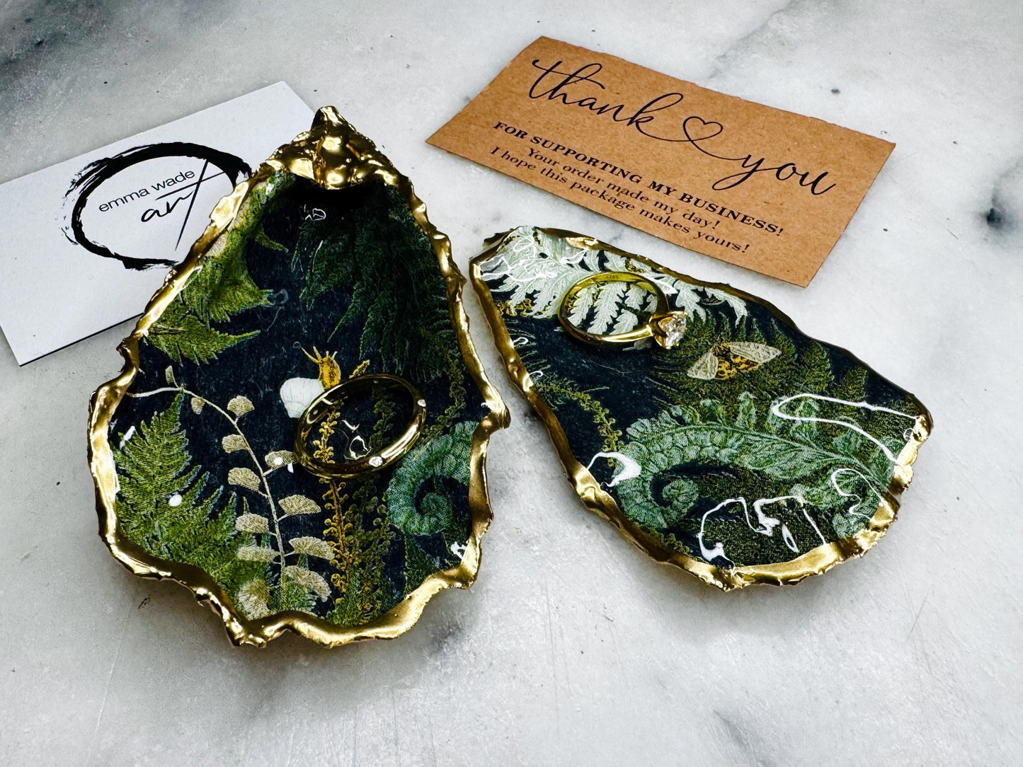 Luxury Dorset oyster shell ring and jewellery box with matching lid, finished with gold leaf detailing and glossy resin. 4 designs avaialble including natural oyster shell with gold rim and pearl interior, gold leaf shell with natural white interior, or gold leaf shell with decoupage interior. Shown holding rings on a light background, highlighting the natural shell shape and polished handcrafted coastal keepsake style. Ideal as an engagement ring box, wedding ring holder, or jewellery keepsake.