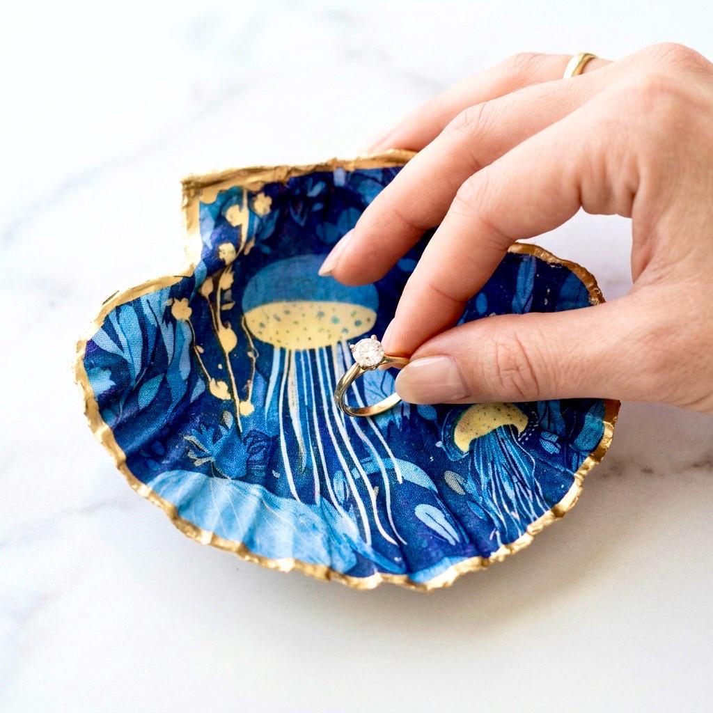 Hand-gilded oyster shell and scallop shell dishes featuring an elegant blue jellyfish design with ocean botanicals, finished with real liquid gold leaf and crystal-clear resin. Coastal ring dishes and jewellery holders available individually or as a matching shell gift set. ✨