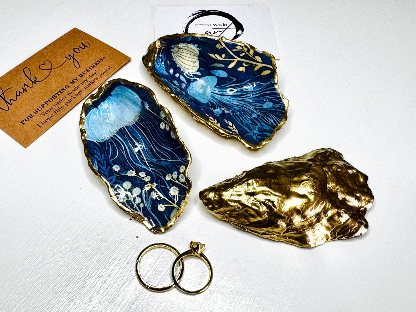 Hand-gilded oyster shell and scallop shell dishes featuring an elegant blue jellyfish design with ocean botanicals, finished with real liquid gold leaf and crystal-clear resin. Coastal ring dishes and jewellery holders available individually or as a matching shell gift set. ✨