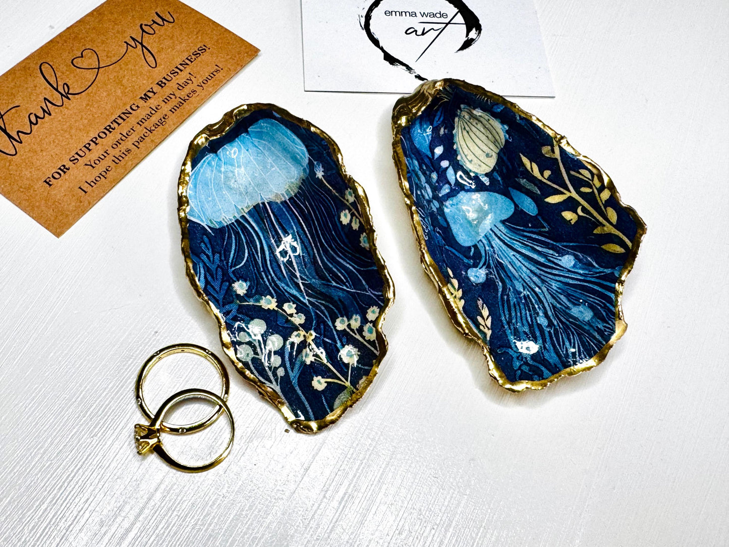Hand-gilded oyster shell and scallop shell dishes featuring an elegant blue jellyfish design with ocean botanicals, finished with real liquid gold leaf and crystal-clear resin. Coastal ring dishes and jewellery holders available individually or as a matching shell gift set. ✨