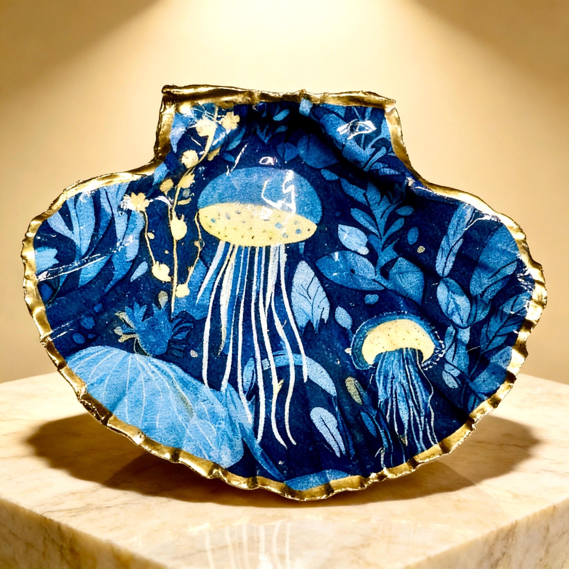 Hand-gilded oyster shell and scallop shell dishes featuring an elegant blue jellyfish design with ocean botanicals, finished with real liquid gold leaf and crystal-clear resin. Coastal ring dishes and jewellery holders available individually or as a matching shell gift set. ✨