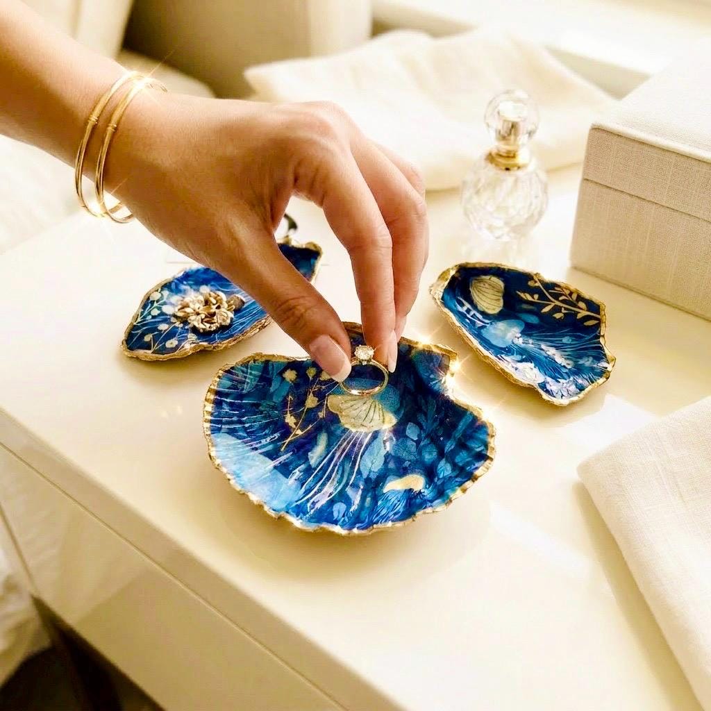 Hand-gilded oyster shell and scallop shell dishes featuring an elegant blue jellyfish design with ocean botanicals, finished with real liquid gold leaf and crystal-clear resin. Coastal ring dishes and jewellery holders available individually or as a matching shell gift set. ✨
