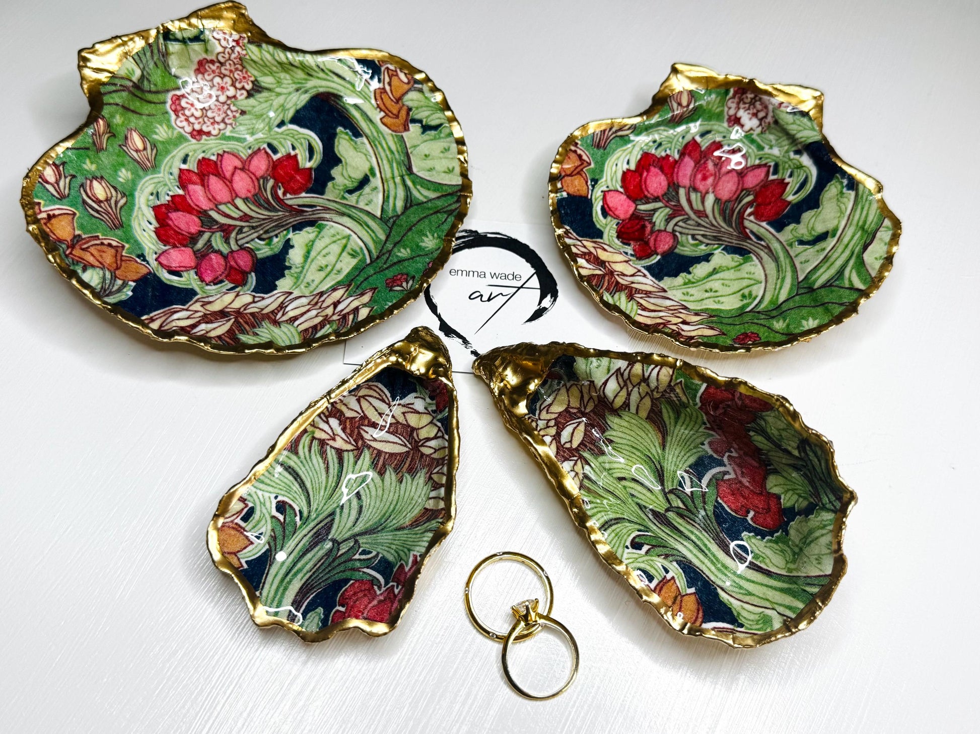 Handcrafted V&A Museum Swirling Trees shell dish collection featuring large and small scallop shells and oyster shells decorated with flowing botanical artwork, pink water lilies and rich green foliage. Each natural Dorset shell is hand-gilded with real liquid gold leaf and sealed with crystal-clear resin. Luxury coastal decor, jewellery dishes, ring holders and trinket trays. Available individually or as a coordinated set of four shells.