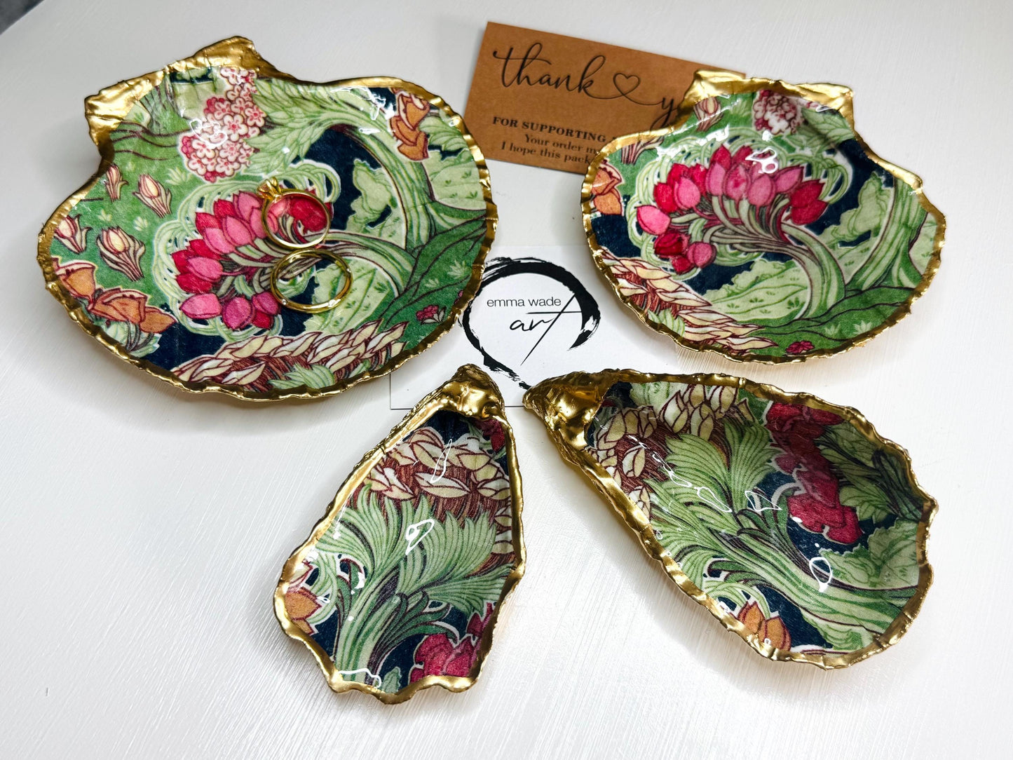 Handcrafted V&A Museum Swirling Trees shell dish collection featuring large and small scallop shells and oyster shells decorated with flowing botanical artwork, pink water lilies and rich green foliage. Each natural Dorset shell is hand-gilded with real liquid gold leaf and sealed with crystal-clear resin. Luxury coastal decor, jewellery dishes, ring holders and trinket trays. Available individually or as a coordinated set of four shells.
