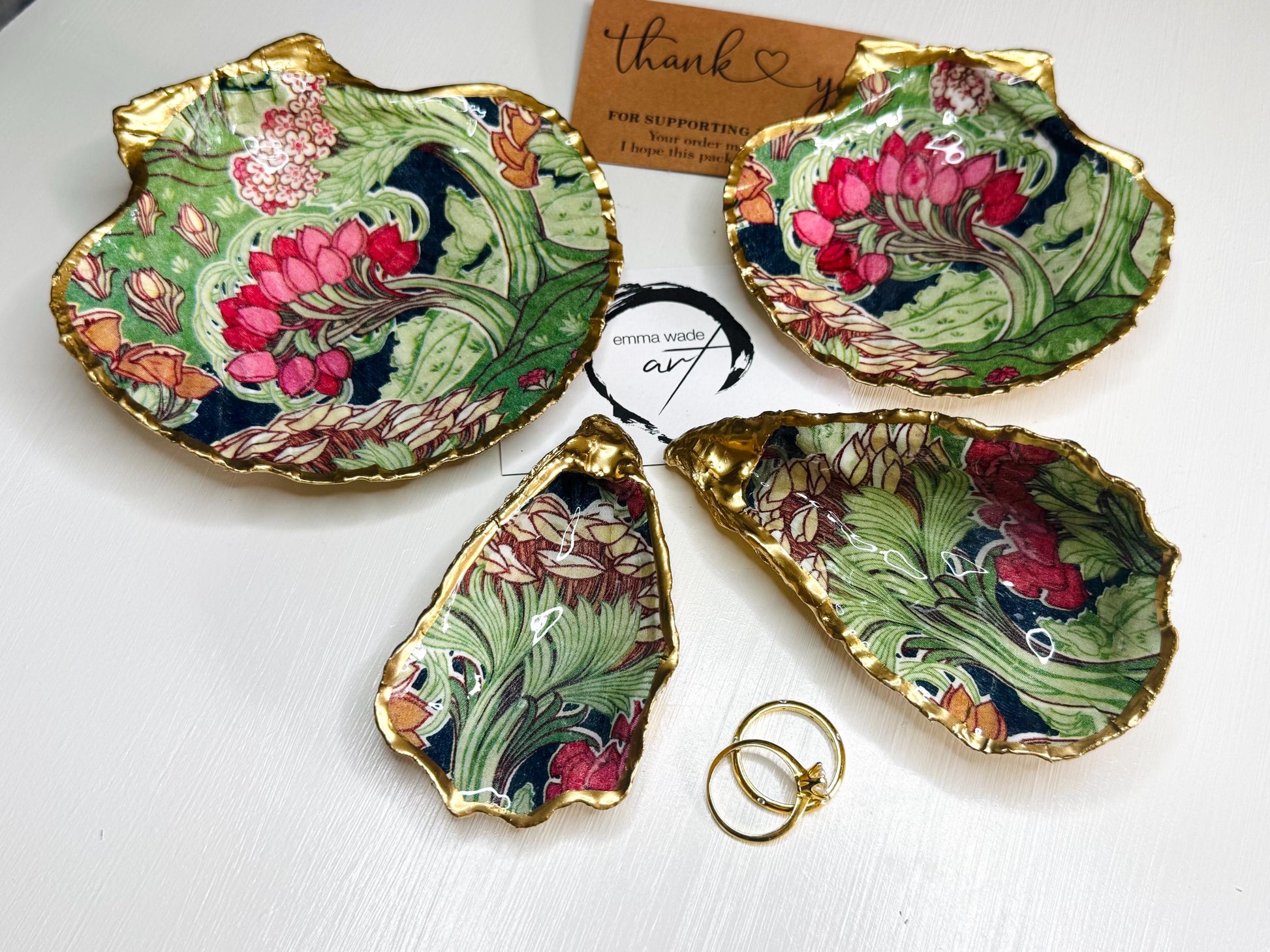 Handcrafted V&A Museum Swirling Trees shell dish collection featuring large and small scallop shells and oyster shells decorated with flowing botanical artwork, pink water lilies and rich green foliage. Each natural Dorset shell is hand-gilded with real liquid gold leaf and sealed with crystal-clear resin. Luxury coastal decor, jewellery dishes, ring holders and trinket trays. Available individually or as a coordinated set of four shells.