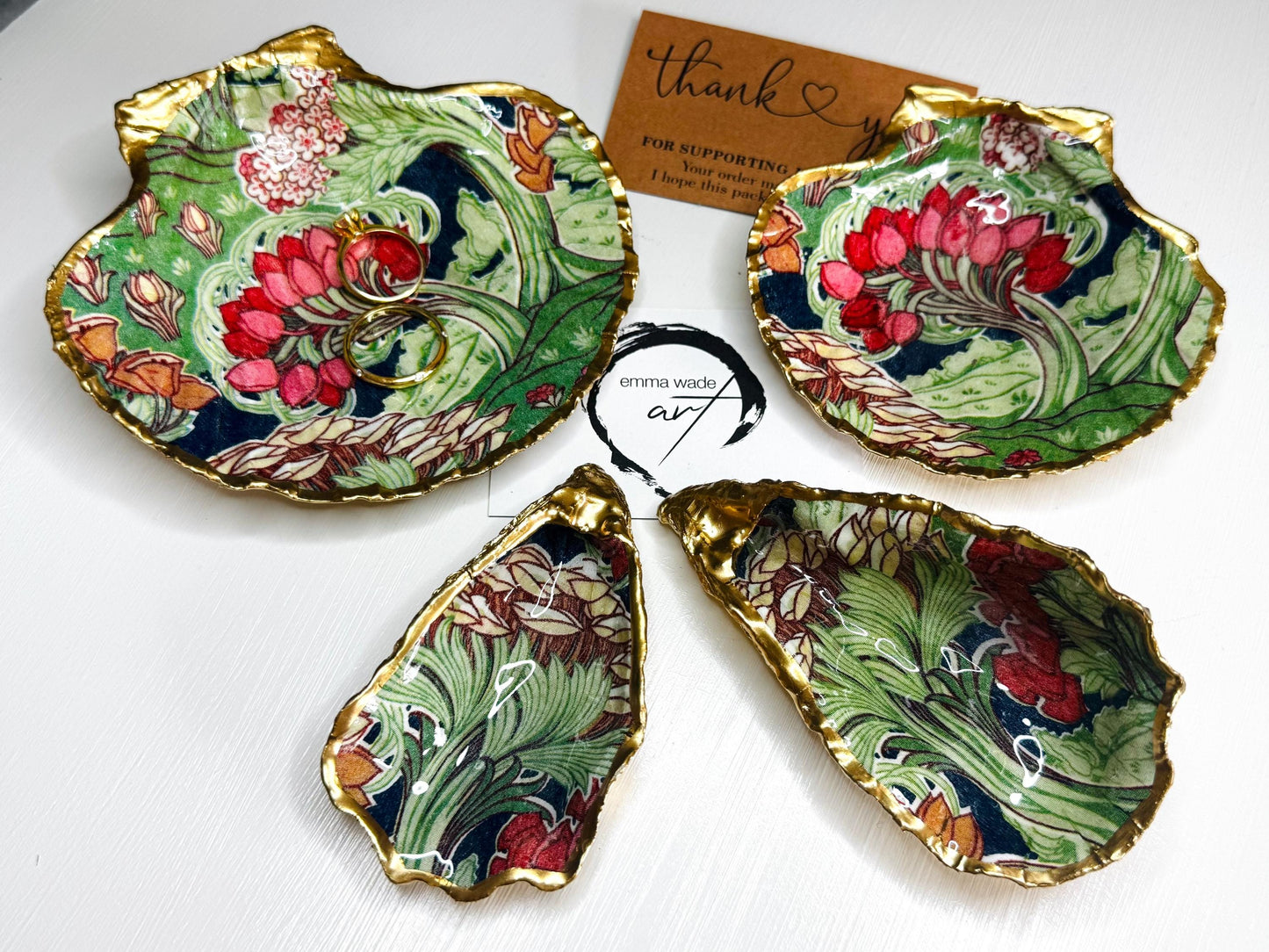 Handcrafted V&A Museum Swirling Trees shell dish collection featuring large and small scallop shells and oyster shells decorated with flowing botanical artwork, pink water lilies and rich green foliage. Each natural Dorset shell is hand-gilded with real liquid gold leaf and sealed with crystal-clear resin. Luxury coastal decor, jewellery dishes, ring holders and trinket trays. Available individually or as a coordinated set of four shells.