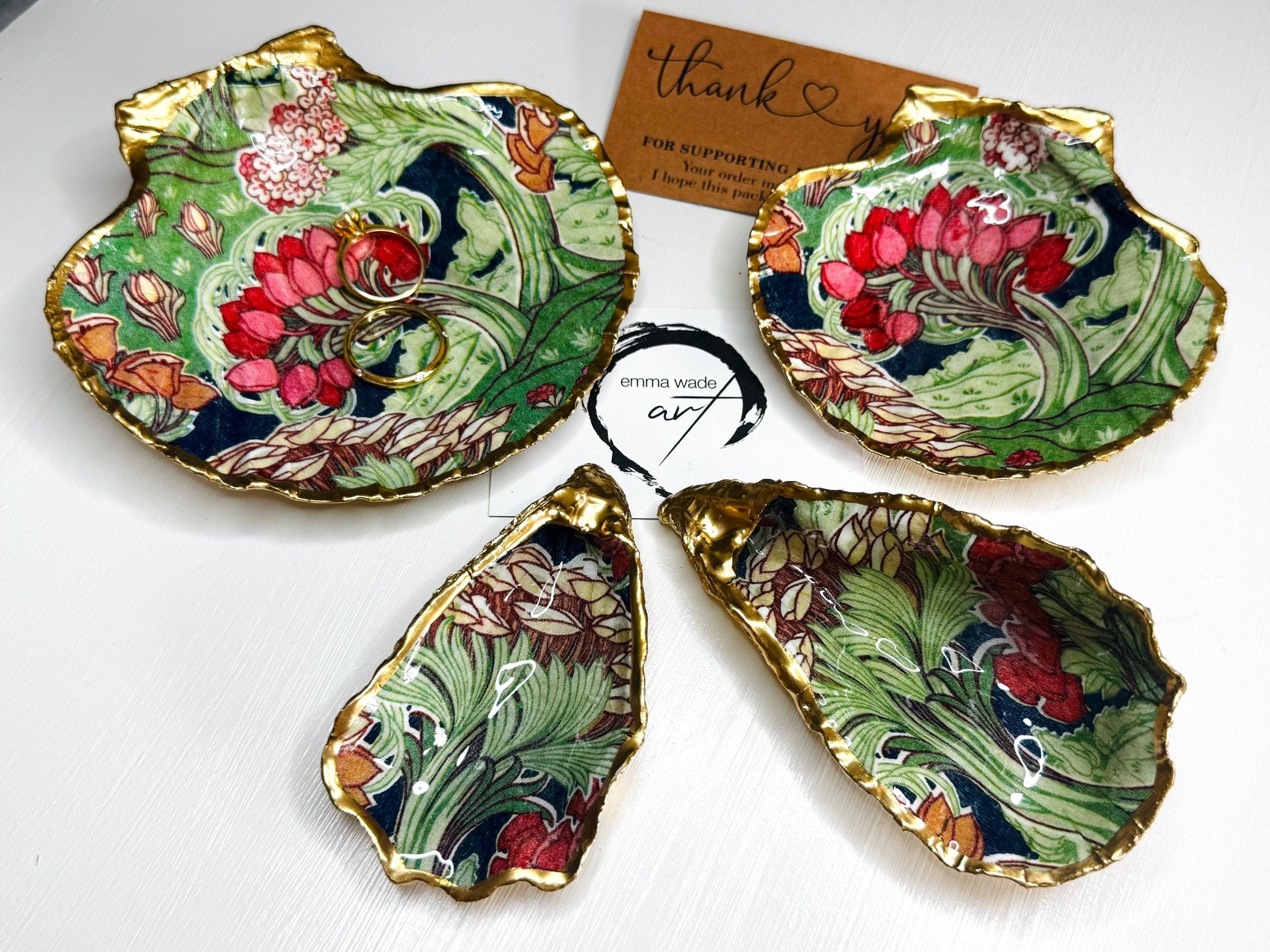Handcrafted V&A Museum Swirling Trees shell dish collection featuring large and small scallop shells and oyster shells decorated with flowing botanical artwork, pink water lilies and rich green foliage. Each natural Dorset shell is hand-gilded with real liquid gold leaf and sealed with crystal-clear resin. Luxury coastal decor, jewellery dishes, ring holders and trinket trays. Available individually or as a coordinated set of four shells.