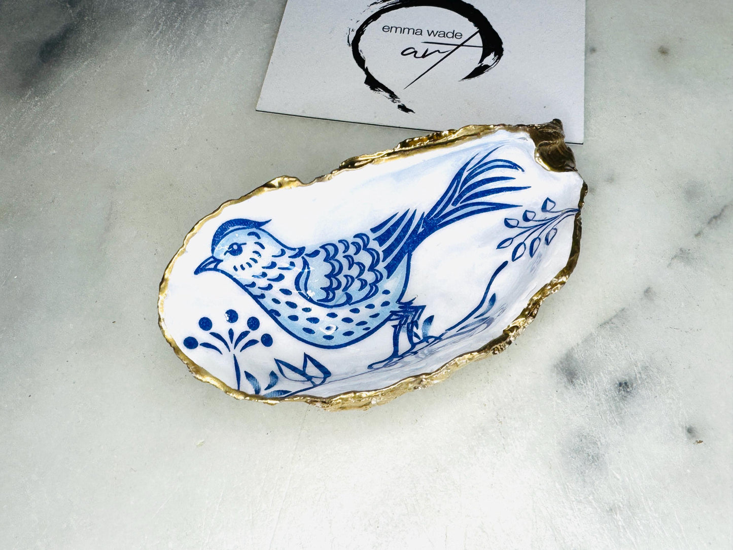 Handmade blue bird oyster shell salt and pepper pinch pot set crafted from natural Dorset oyster shells with glossy pearlescent interiors, blue porcelain style bird artwork and shimmering liquid gold leaf edging. Luxury coastal cruet dishes sealed with food-safe resin and styled with optional gold spoons. Elegant seaside dining decor for beach house kitchens, dinner parties, weddings, anniversaries and bird lovers. Artisan shell tableware handmade in the UK with coastal blue and white styling.