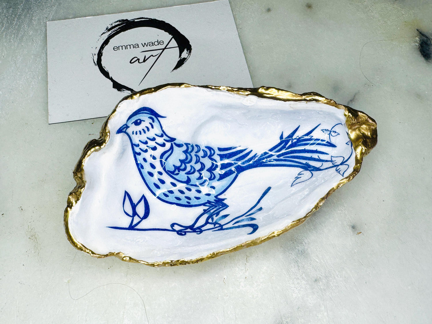 Handmade blue bird oyster shell salt and pepper pinch pot set crafted from natural Dorset oyster shells with glossy pearlescent interiors, blue porcelain style bird artwork and shimmering liquid gold leaf edging. Luxury coastal cruet dishes sealed with food-safe resin and styled with optional gold spoons. Elegant seaside dining decor for beach house kitchens, dinner parties, weddings, anniversaries and bird lovers. Artisan shell tableware handmade in the UK with coastal blue and white styling.