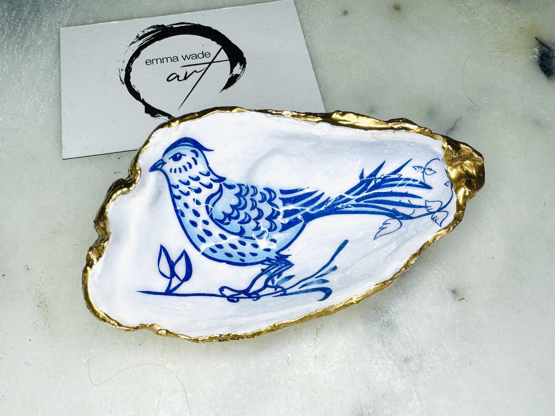 Handmade blue bird oyster shell salt and pepper pinch pot set crafted from natural Dorset oyster shells with glossy pearlescent interiors, blue porcelain style bird artwork and shimmering liquid gold leaf edging. Luxury coastal cruet dishes sealed with food-safe resin and styled with optional gold spoons. Elegant seaside dining decor for beach house kitchens, dinner parties, weddings, anniversaries and bird lovers. Artisan shell tableware handmade in the UK with coastal blue and white styling.