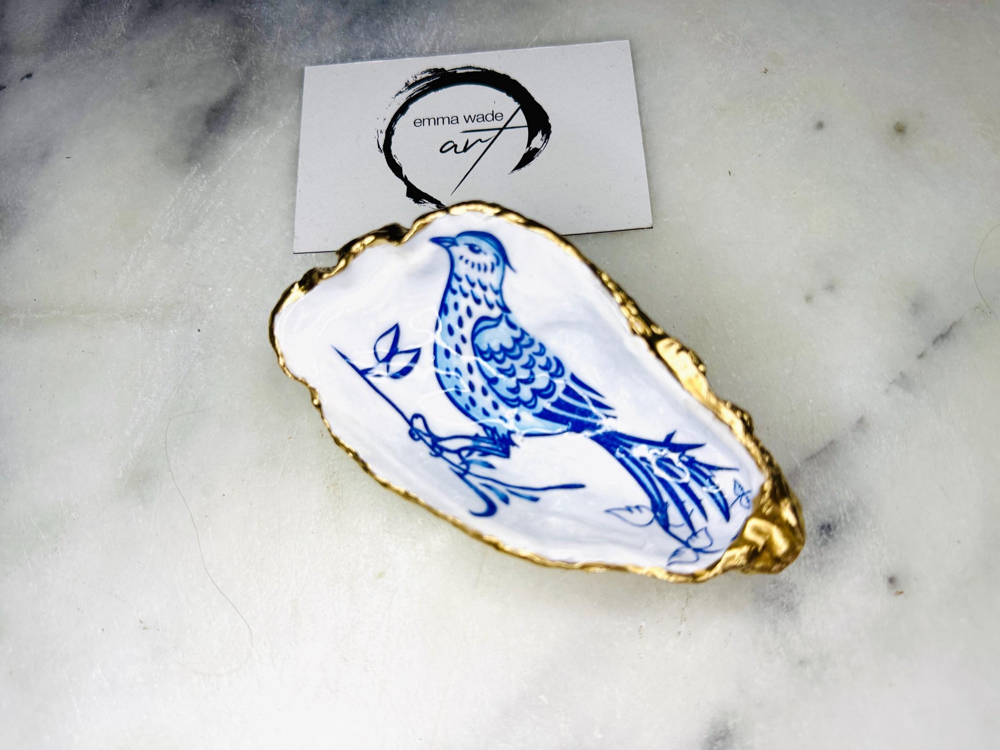 Handmade blue bird oyster shell salt and pepper pinch pot set crafted from natural Dorset oyster shells with glossy pearlescent interiors, blue porcelain style bird artwork and shimmering liquid gold leaf edging. Luxury coastal cruet dishes sealed with food-safe resin and styled with optional gold spoons. Elegant seaside dining decor for beach house kitchens, dinner parties, weddings, anniversaries and bird lovers. Artisan shell tableware handmade in the UK with coastal blue and white styling.
