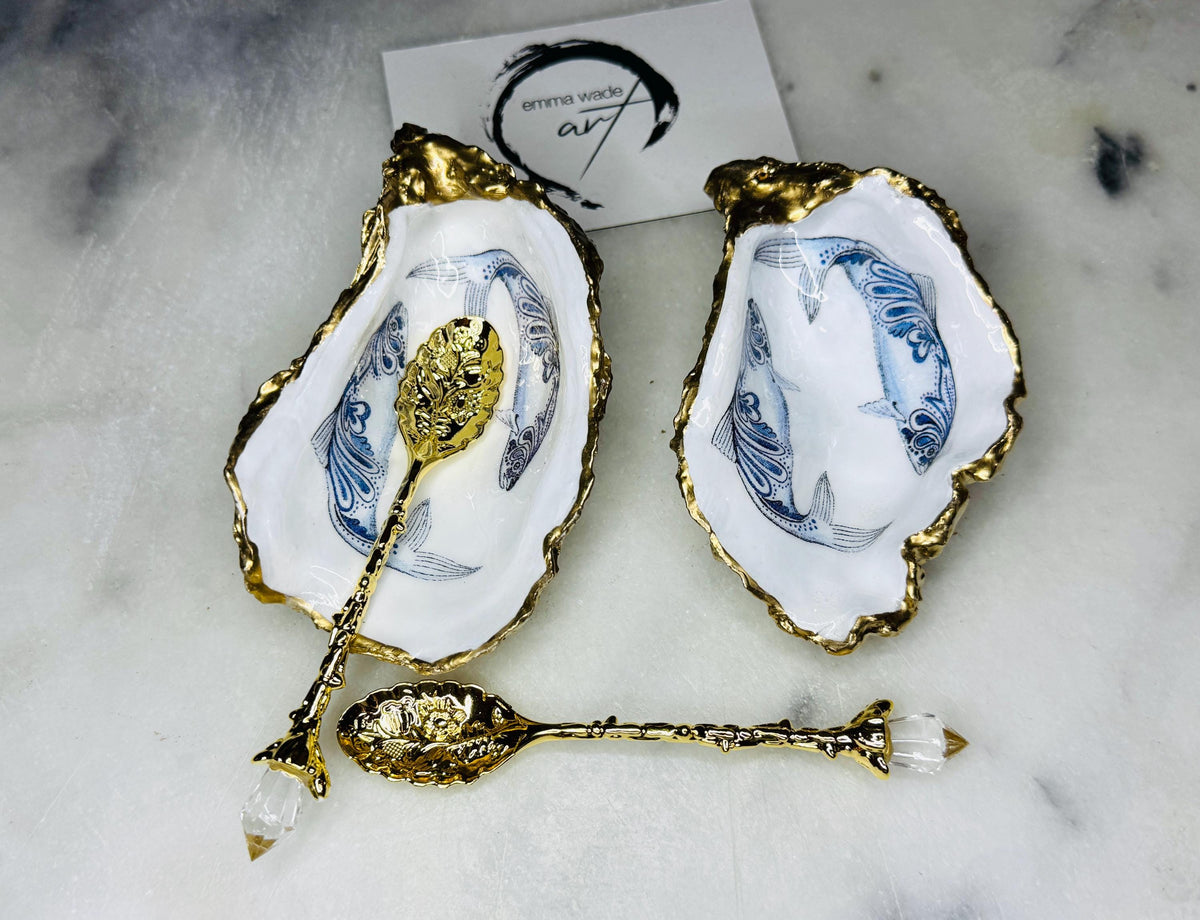 Handmade Dorset oyster shell salt and pepper pinch pots featuring blue paisley fish designs with gold leaf edging and glossy resin finish. Coastal oyster shell cruet set with natural pearlescent interiors and optional gold spoons, styled as elegant nautical table décor and condiment dishes.