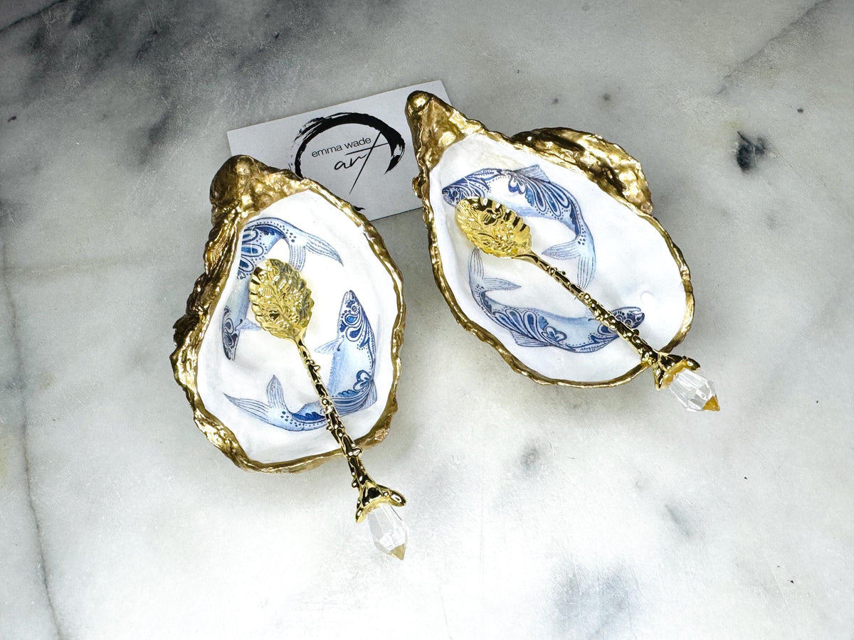 Handmade Dorset oyster shell salt and pepper pinch pots featuring blue paisley fish designs with gold leaf edging and glossy resin finish. Coastal oyster shell cruet set with natural pearlescent interiors and optional gold spoons, styled as elegant nautical table décor and condiment dishes.