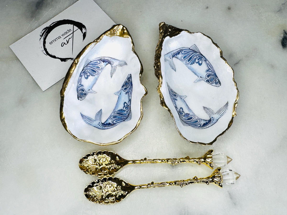 Handmade Dorset oyster shell salt and pepper pinch pots featuring blue paisley fish designs with gold leaf edging and glossy resin finish. Coastal oyster shell cruet set with natural pearlescent interiors and optional gold spoons, styled as elegant nautical table décor and condiment dishes.