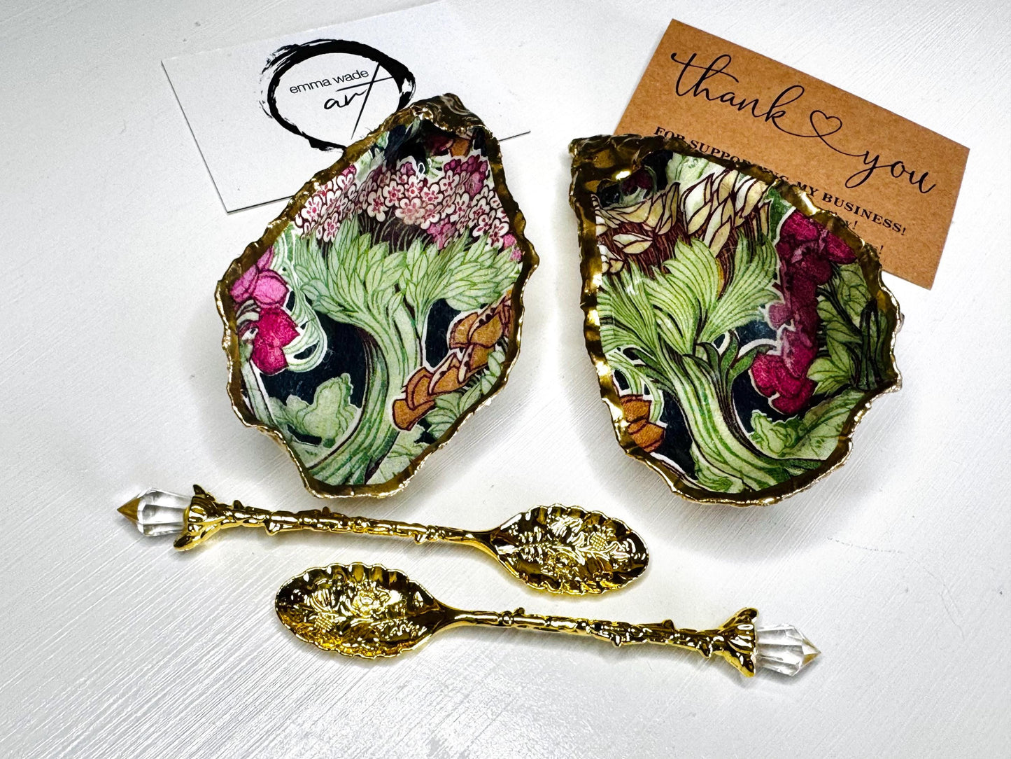 Handcrafted pair of oyster shell salt and pepper pinch pots featuring the Forest Trees botanical design in rich green, pink, cream and gold tones. Natural Dorset oyster shells hand-finished with liquid gold leaf edging and sealed beneath a crystal-clear resin for a glossy finish. Includes optional gold crystal spoons. Elegant table decor for dining, entertaining, weddings, anniversaries and housewarming gifts. Handmade in Surrey, England by Emma Wade ART.