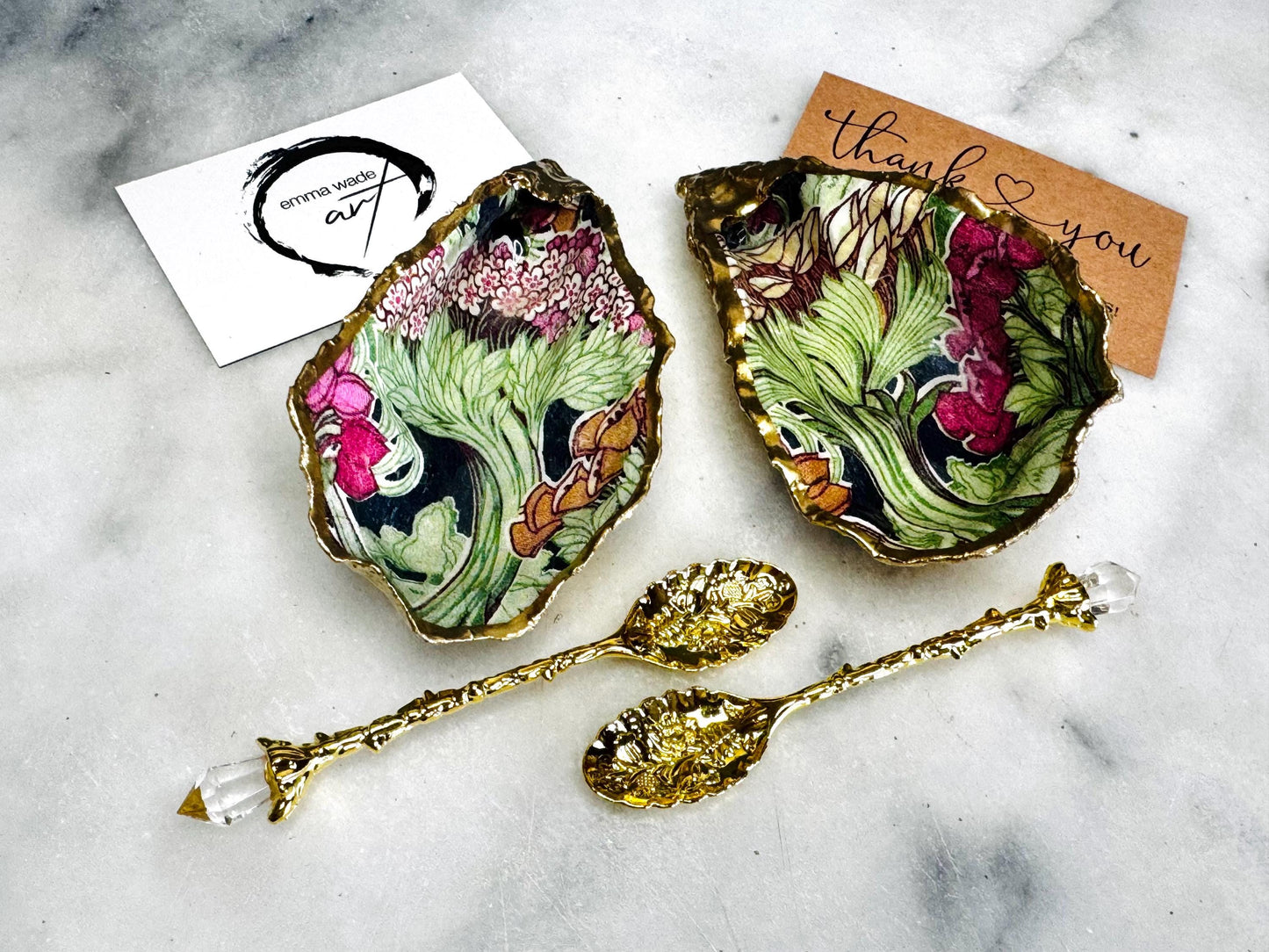 Handcrafted pair of oyster shell salt and pepper pinch pots featuring the Forest Trees botanical design in rich green, pink, cream and gold tones. Natural Dorset oyster shells hand-finished with liquid gold leaf edging and sealed beneath a crystal-clear resin for a glossy finish. Includes optional gold crystal spoons. Elegant table decor for dining, entertaining, weddings, anniversaries and housewarming gifts. Handmade in Surrey, England by Emma Wade ART.