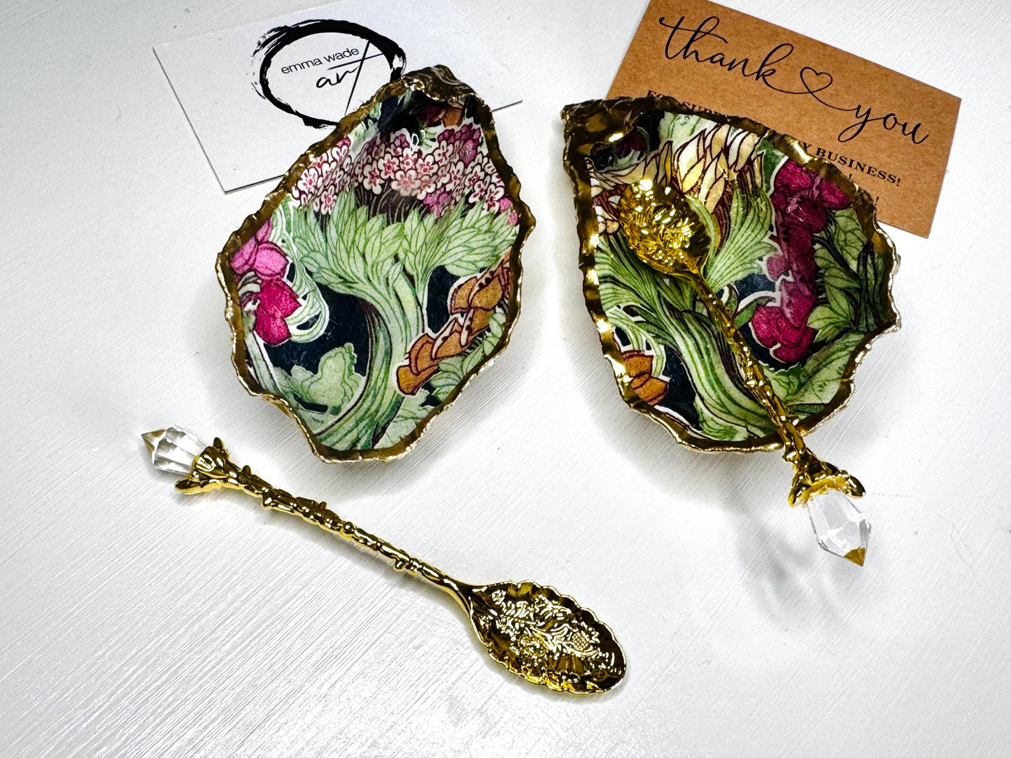 Handcrafted pair of oyster shell salt and pepper pinch pots featuring the Forest Trees botanical design in rich green, pink, cream and gold tones. Natural Dorset oyster shells hand-finished with liquid gold leaf edging and sealed beneath a crystal-clear resin for a glossy finish. Includes optional gold crystal spoons. Elegant table decor for dining, entertaining, weddings, anniversaries and housewarming gifts. Handmade in Surrey, England by Emma Wade ART.