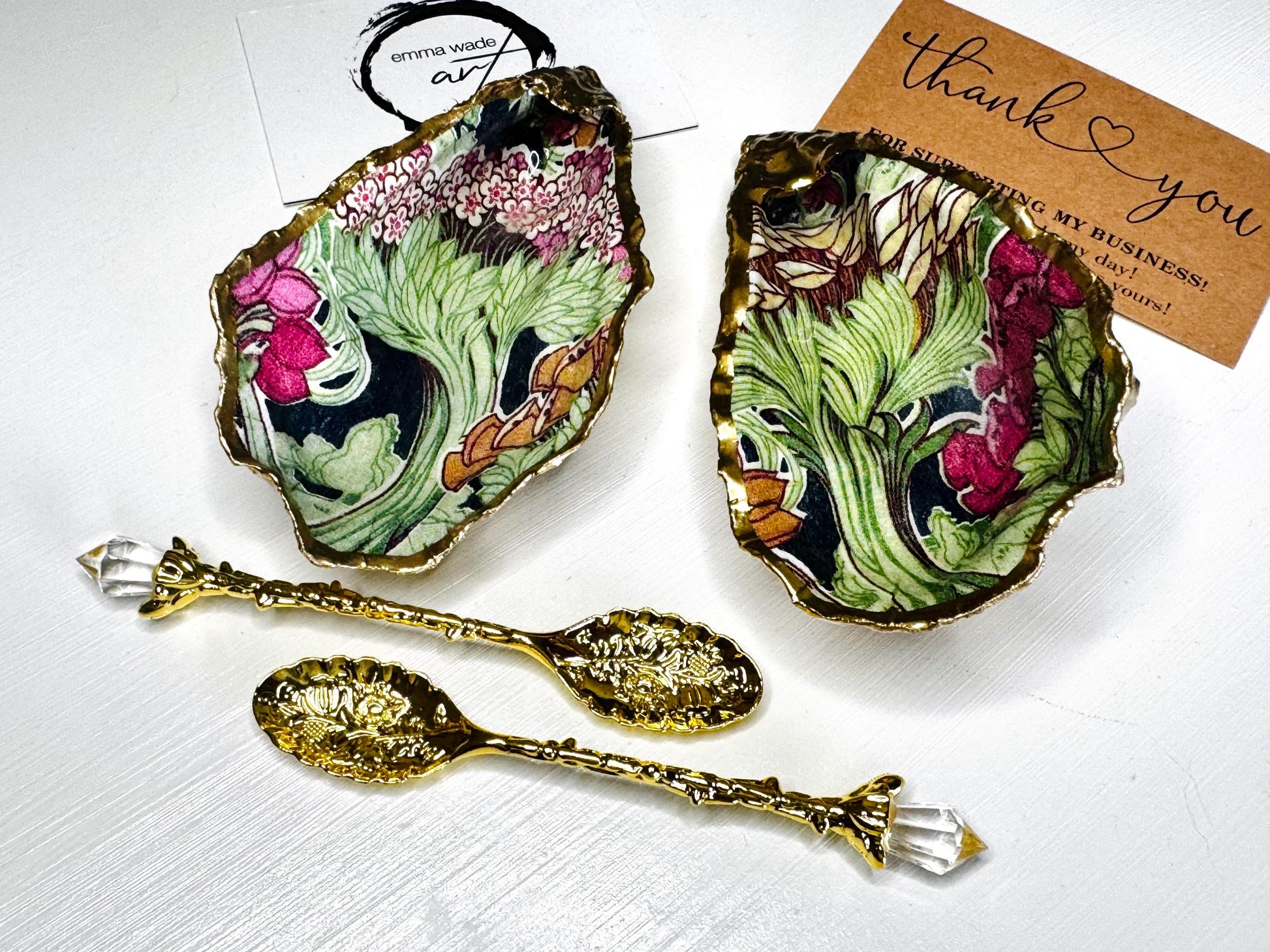 Handcrafted pair of oyster shell salt and pepper pinch pots featuring the Forest Trees botanical design in rich green, pink, cream and gold tones. Natural Dorset oyster shells hand-finished with liquid gold leaf edging and sealed beneath a crystal-clear resin for a glossy finish. Includes optional gold crystal spoons. Elegant table decor for dining, entertaining, weddings, anniversaries and housewarming gifts. Handmade in Surrey, England by Emma Wade ART.