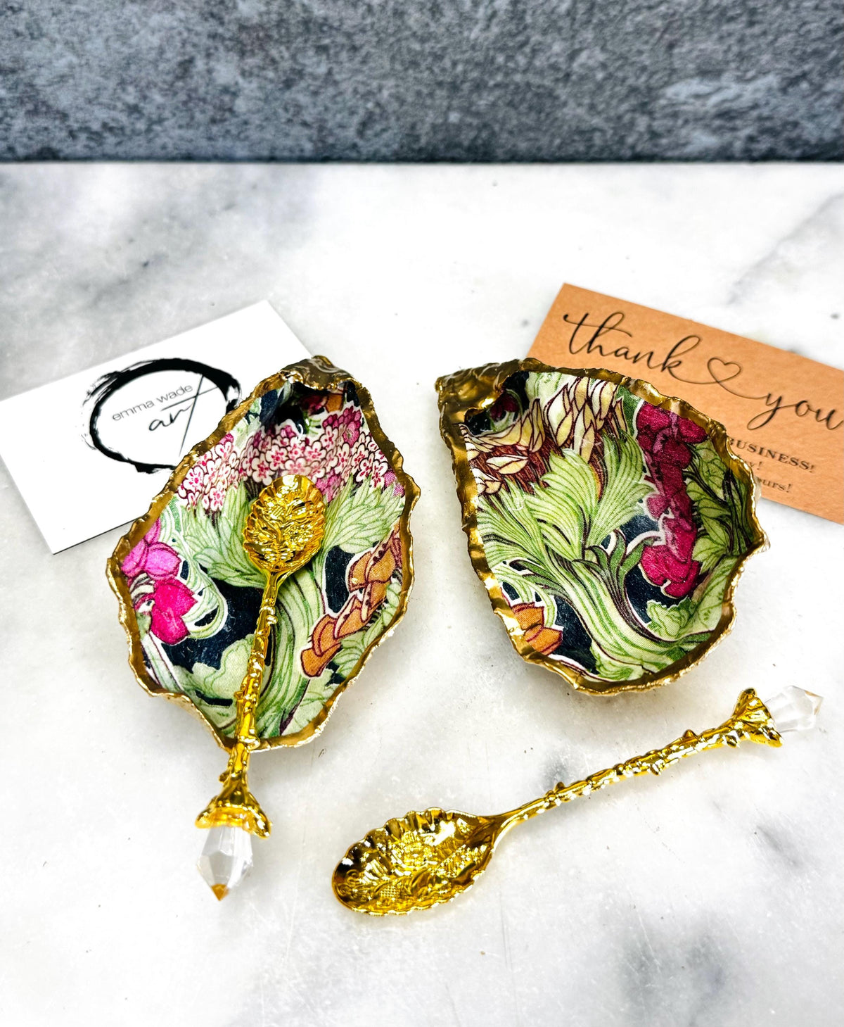 Handcrafted pair of oyster shell salt and pepper pinch pots featuring the Forest Trees botanical design in rich green, pink, cream and gold tones. Natural Dorset oyster shells hand-finished with liquid gold leaf edging and sealed beneath a crystal-clear resin for a glossy finish. Includes optional gold crystal spoons. Elegant table decor for dining, entertaining, weddings, anniversaries and housewarming gifts. Handmade in Surrey, England by Emma Wade ART.