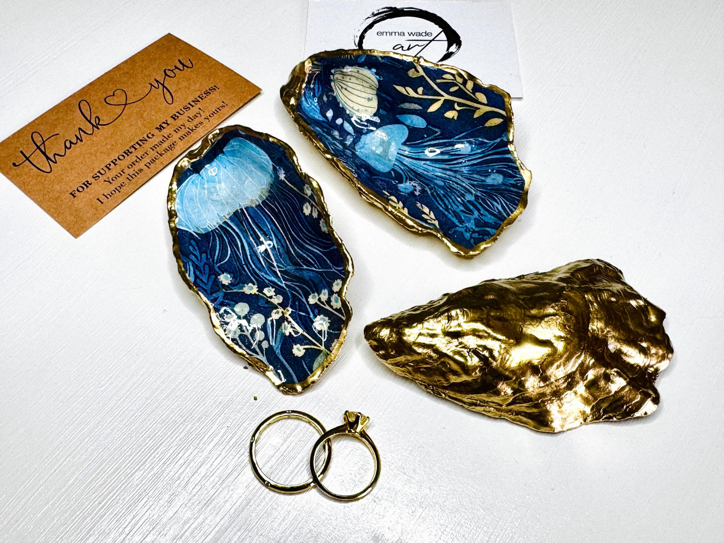 Hand-gilded oyster shell and scallop shell dishes featuring an elegant blue jellyfish design with ocean botanicals, finished with real liquid gold leaf and crystal-clear resin. Coastal ring dishes and jewellery holders available individually or as a matching shell gift set. ✨