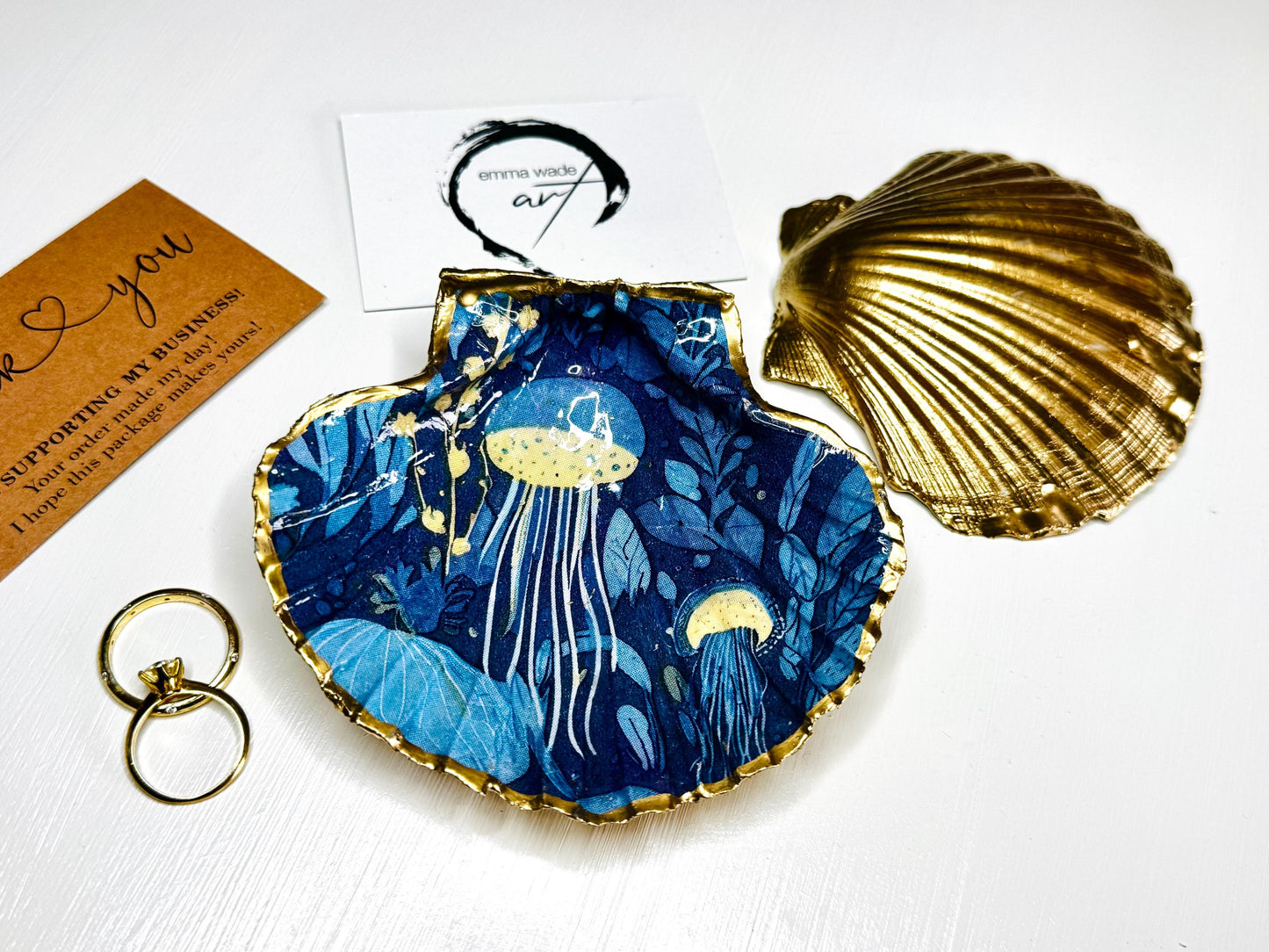 Hand-gilded oyster shell and scallop shell dishes featuring an elegant blue jellyfish design with ocean botanicals, finished with real liquid gold leaf and crystal-clear resin. Coastal ring dishes and jewellery holders available individually or as a matching shell gift set. ✨