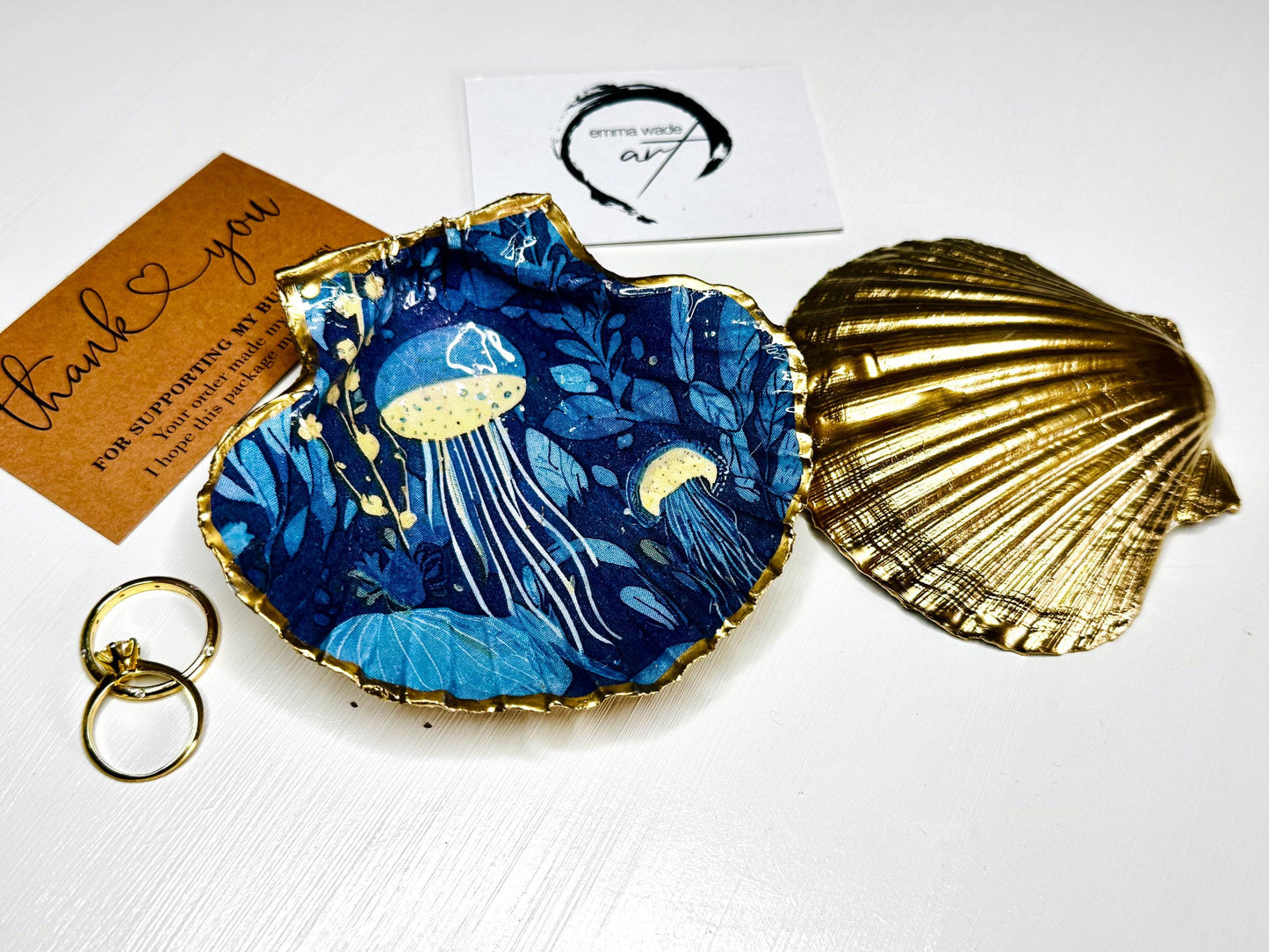 Hand-gilded oyster shell and scallop shell dishes featuring an elegant blue jellyfish design with ocean botanicals, finished with real liquid gold leaf and crystal-clear resin. Coastal ring dishes and jewellery holders available individually or as a matching shell gift set. ✨