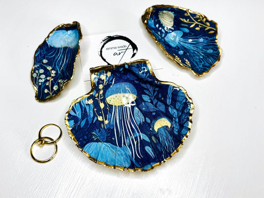Hand-gilded oyster shell and scallop shell dishes featuring an elegant blue jellyfish design with ocean botanicals, finished with real liquid gold leaf and crystal-clear resin. Coastal ring dishes and jewellery holders available individually or as a matching shell gift set. ✨