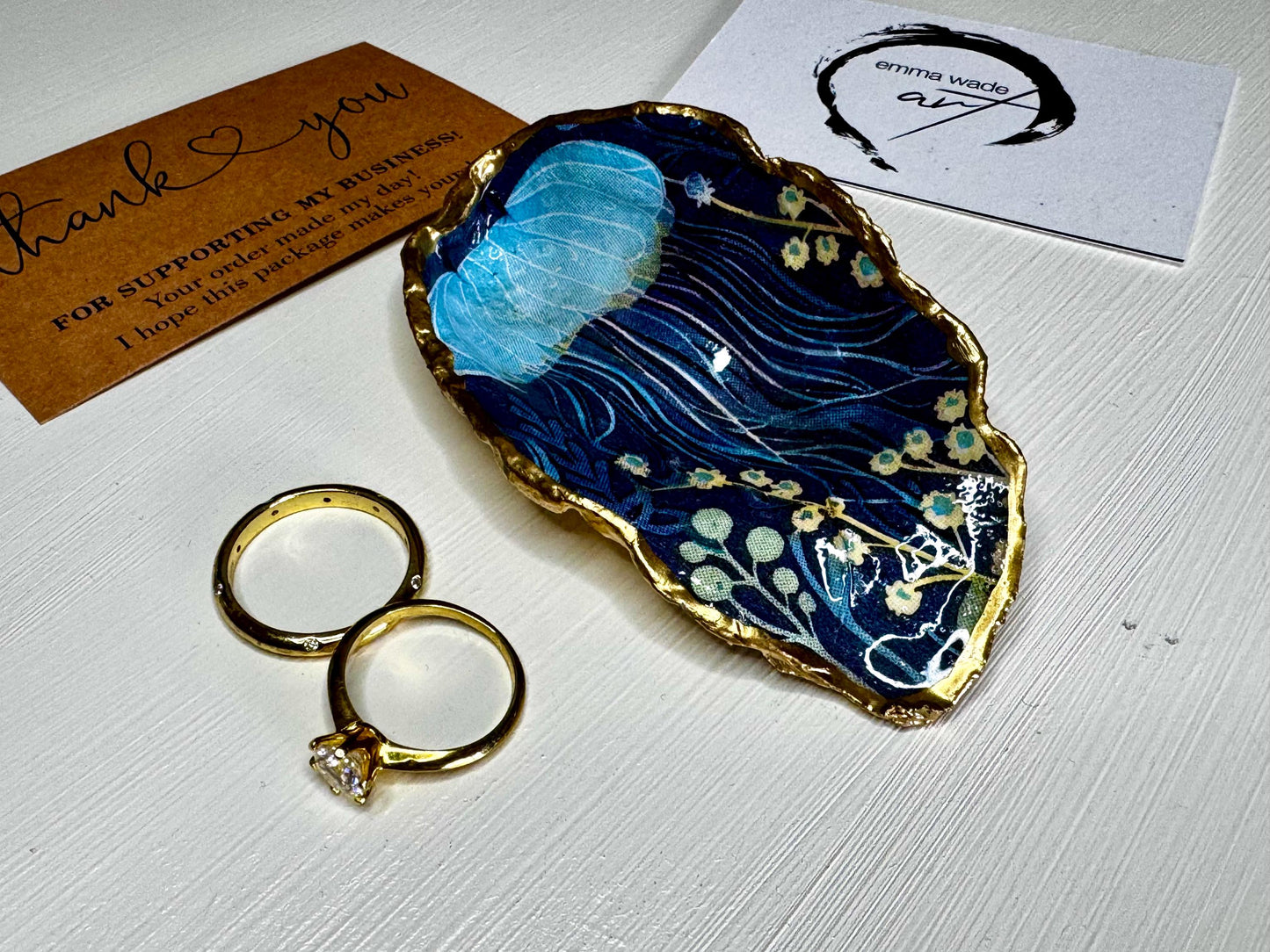Hand-gilded oyster shell and scallop shell dishes featuring an elegant blue jellyfish design with ocean botanicals, finished with real liquid gold leaf and crystal-clear resin. Coastal ring dishes and jewellery holders available individually or as a matching shell gift set. ✨