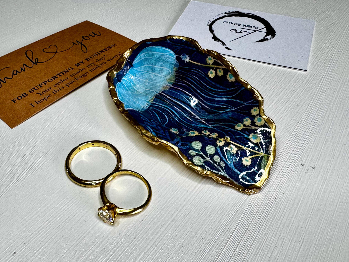 Hand-gilded oyster shell and scallop shell dishes featuring an elegant blue jellyfish design with ocean botanicals, finished with real liquid gold leaf and crystal-clear resin. Coastal ring dishes and jewellery holders available individually or as a matching shell gift set. ✨