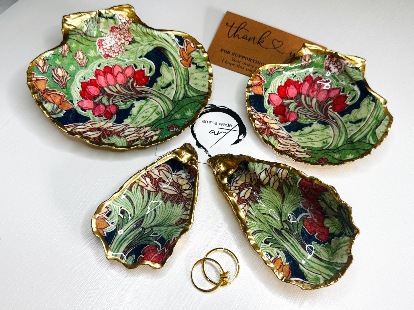 Handcrafted V&A Museum Swirling Trees shell dish collection featuring large and small scallop shells and oyster shells decorated with flowing botanical artwork, pink water lilies and rich green foliage. Each natural Dorset shell is hand-gilded with real liquid gold leaf and sealed with crystal-clear resin. Luxury coastal decor, jewellery dishes, ring holders and trinket trays. Available individually or as a coordinated set of four shells.