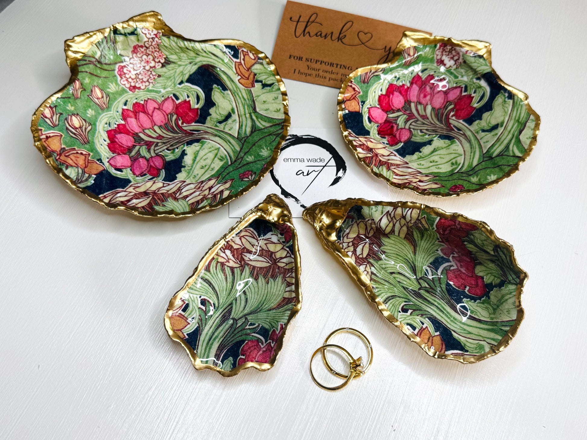 Handcrafted V&A Museum Swirling Trees shell dish collection featuring large and small scallop shells and oyster shells decorated with flowing botanical artwork, pink water lilies and rich green foliage. Each natural Dorset shell is hand-gilded with real liquid gold leaf and sealed with crystal-clear resin. Luxury coastal decor, jewellery dishes, ring holders and trinket trays. Available individually or as a coordinated set of four shells.