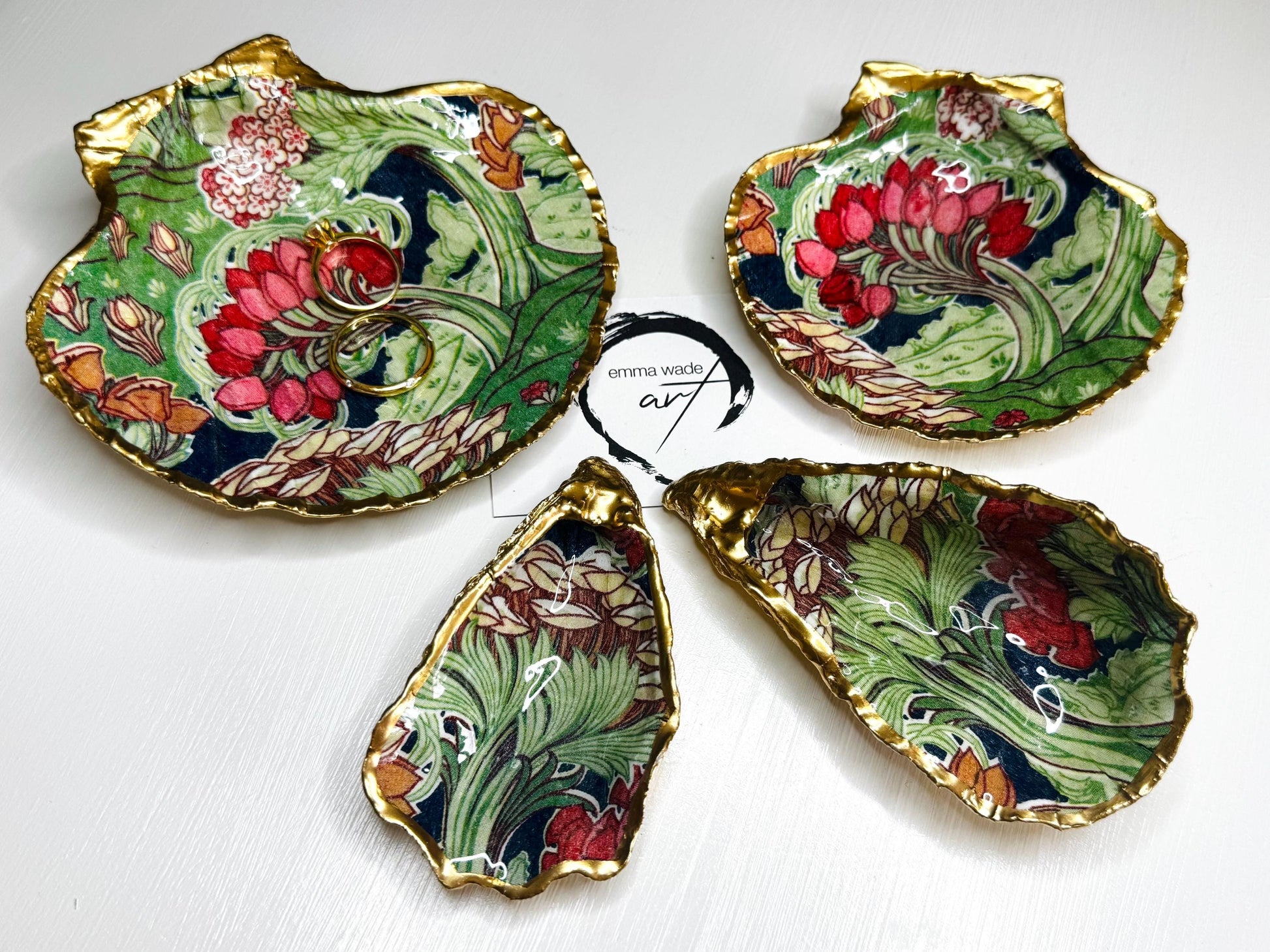 Handcrafted V&A Museum Swirling Trees shell dish collection featuring large and small scallop shells and oyster shells decorated with flowing botanical artwork, pink water lilies and rich green foliage. Each natural Dorset shell is hand-gilded with real liquid gold leaf and sealed with crystal-clear resin. Luxury coastal decor, jewellery dishes, ring holders and trinket trays. Available individually or as a coordinated set of four shells.