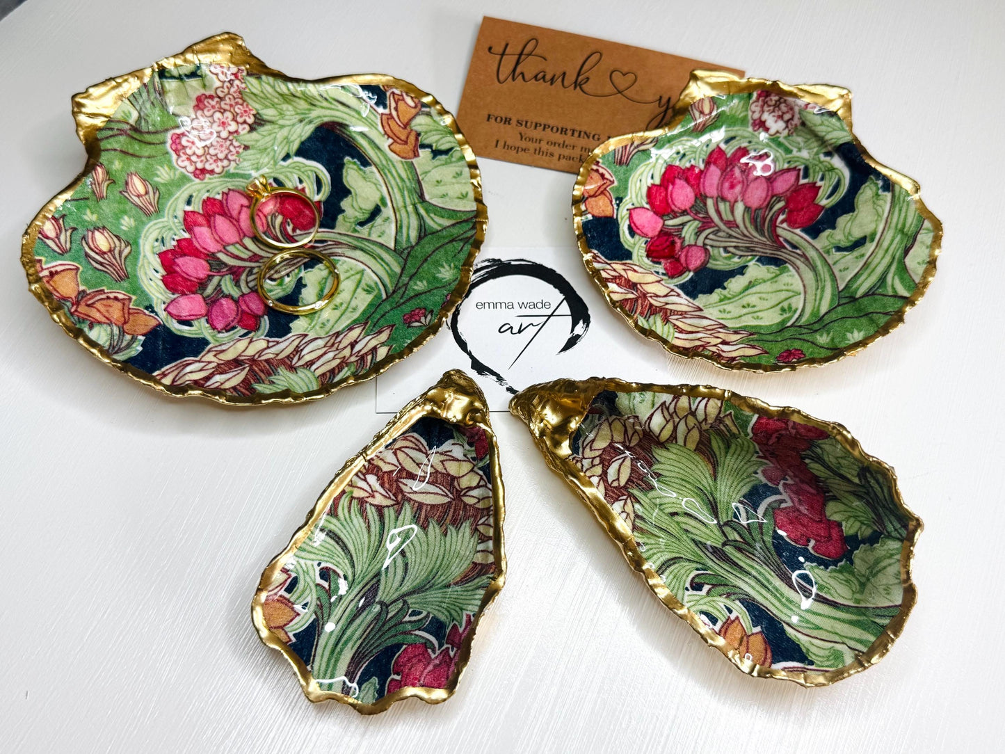 Handcrafted V&A Museum Swirling Trees shell dish collection featuring large and small scallop shells and oyster shells decorated with flowing botanical artwork, pink water lilies and rich green foliage. Each natural Dorset shell is hand-gilded with real liquid gold leaf and sealed with crystal-clear resin. Luxury coastal decor, jewellery dishes, ring holders and trinket trays. Available individually or as a coordinated set of four shells.
