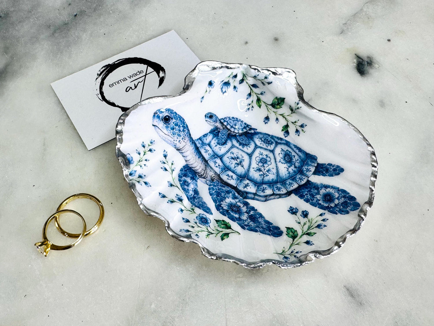 Sea Turtle Mum and Baby scallop shell trinket dish featuring an original illustrated Delft Blue design by Emma Wade ART. Natural scallop shell finished with gold leaf or silver leaf edging and a crystal-clear glossy resin coating. Coastal jewellery tray, ring holder and ocean-inspired gift for sea turtle lovers, beach house décor, weddings, bridesmaids and nautical homes.