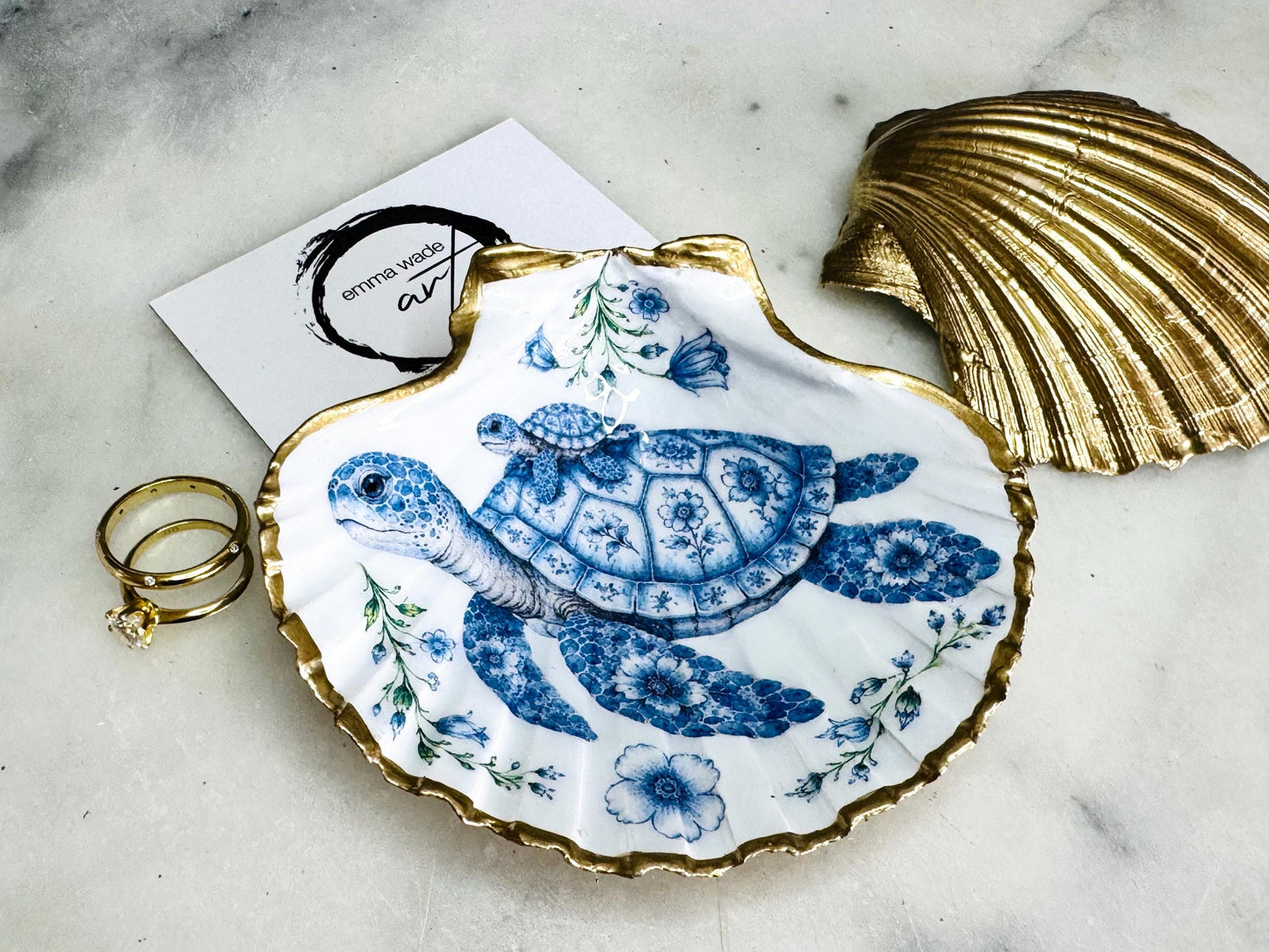 Sea Turtle Mum and Baby scallop shell trinket dish featuring an original illustrated Delft Blue design by Emma Wade ART. Natural scallop shell finished with gold leaf or silver leaf edging and a crystal-clear glossy resin coating. Coastal jewellery tray, ring holder and ocean-inspired gift for sea turtle lovers, beach house décor, weddings, bridesmaids and nautical homes.