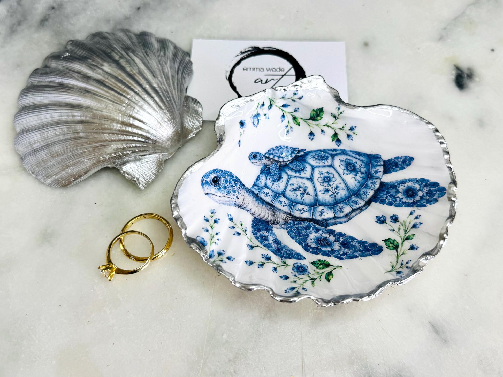 Sea Turtle Mum and Baby scallop shell trinket dish featuring an original illustrated Delft Blue design by Emma Wade ART. Natural scallop shell finished with gold leaf or silver leaf edging and a crystal-clear glossy resin coating. Coastal jewellery tray, ring holder and ocean-inspired gift for sea turtle lovers, beach house décor, weddings, bridesmaids and nautical homes.