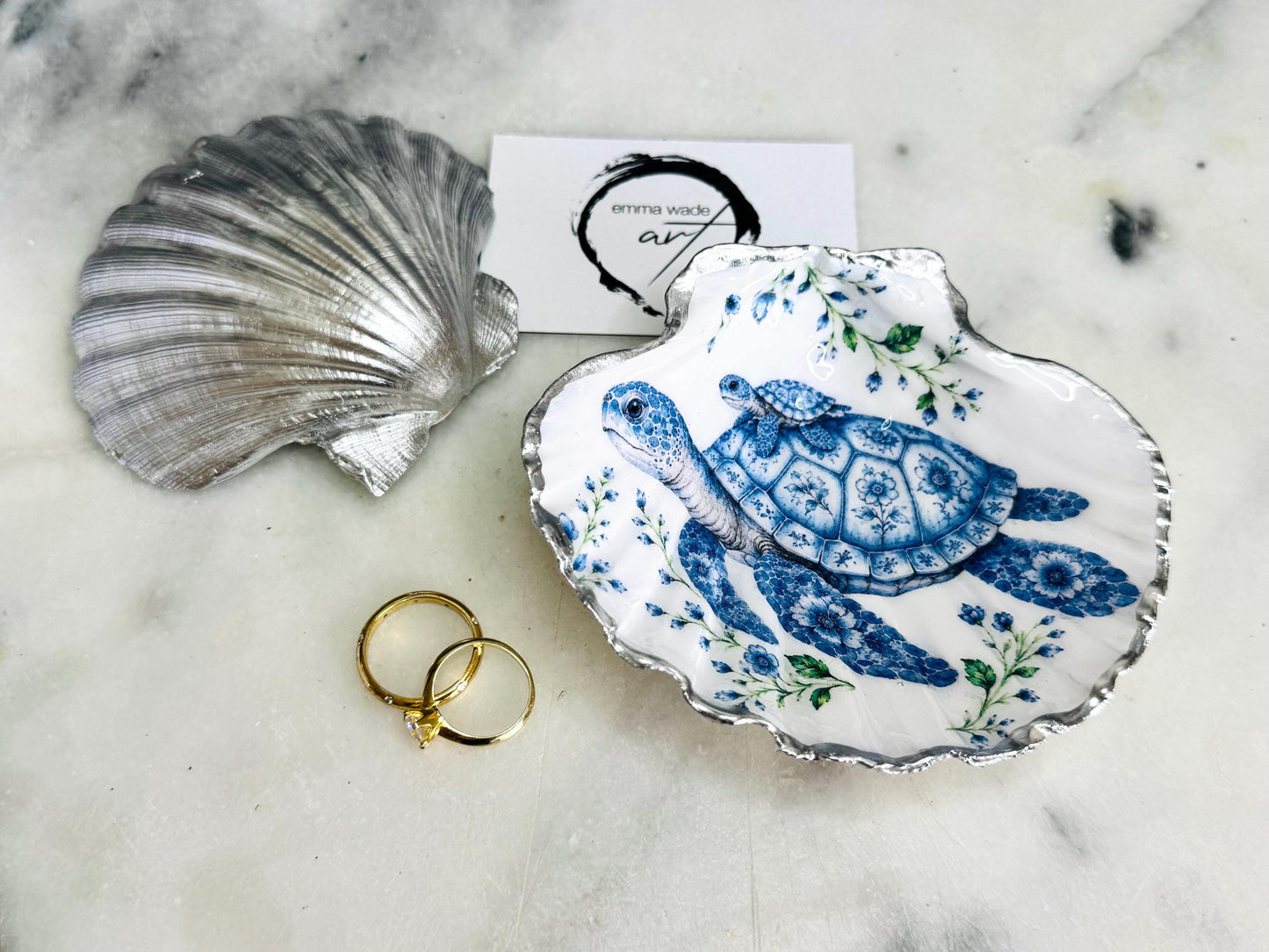 Sea Turtle Mum and Baby scallop shell trinket dish featuring an original illustrated Delft Blue design by Emma Wade ART. Natural scallop shell finished with gold leaf or silver leaf edging and a crystal-clear glossy resin coating. Coastal jewellery tray, ring holder and ocean-inspired gift for sea turtle lovers, beach house décor, weddings, bridesmaids and nautical homes.