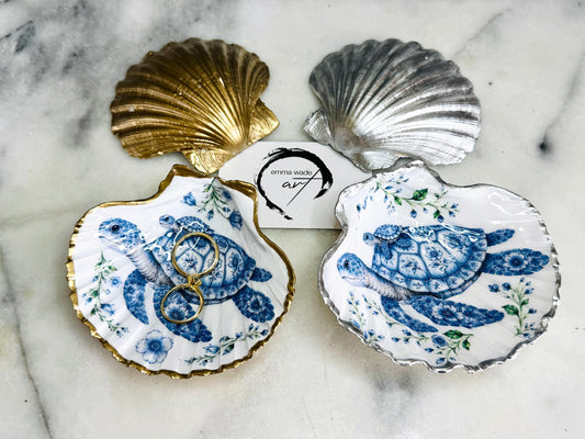Sea Turtle Mum and Baby scallop shell trinket dish featuring an original illustrated Delft Blue design by Emma Wade ART. Natural scallop shell finished with gold leaf or silver leaf edging and a crystal-clear glossy resin coating. Coastal jewellery tray, ring holder and ocean-inspired gift for sea turtle lovers, beach house décor, weddings, bridesmaids and nautical homes.