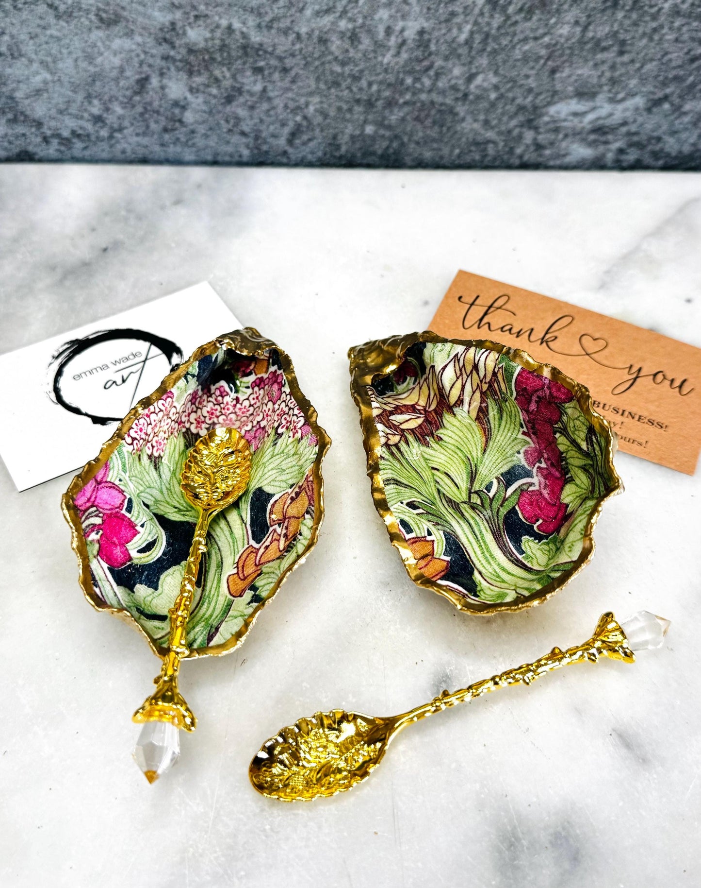 Handcrafted pair of oyster shell salt and pepper pinch pots featuring the Forest Trees botanical design in rich green, pink, cream and gold tones. Natural Dorset oyster shells hand-finished with liquid gold leaf edging and sealed beneath a crystal-clear resin for a glossy finish. Includes optional gold crystal spoons. Elegant table decor for dining, entertaining, weddings, anniversaries and housewarming gifts. Handmade in Surrey, England by Emma Wade ART.