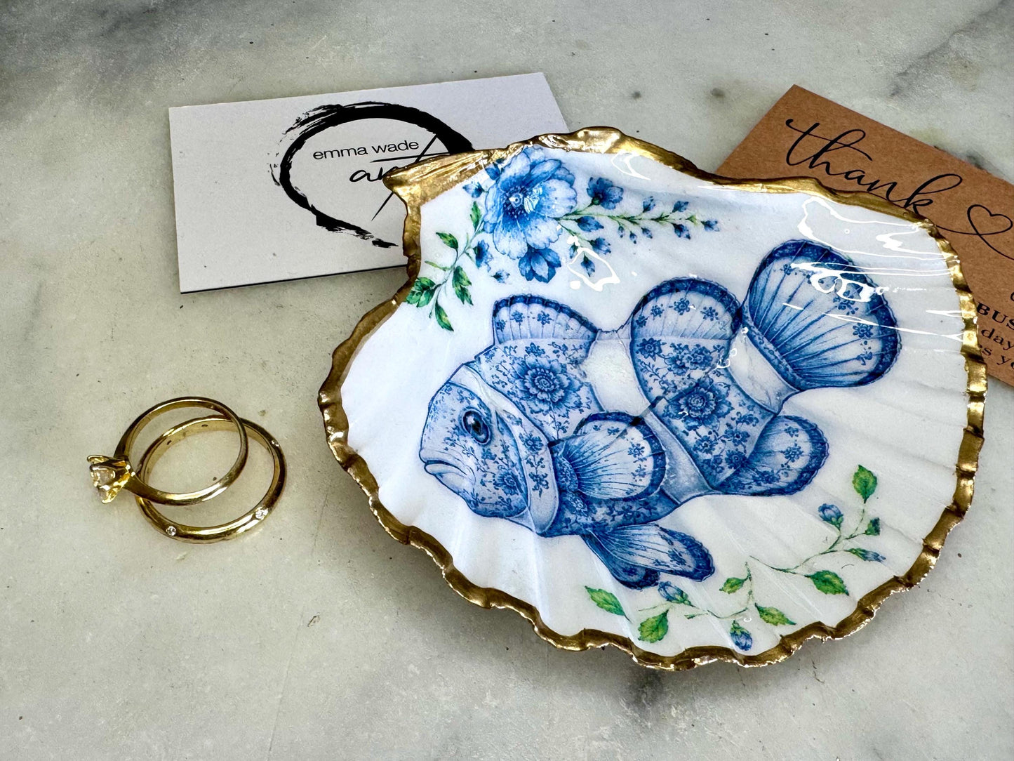 Clownfish scallop shell trinket dish featuring an original illustrated Delft Blue design by Emma Wade ART. Natural scallop shell finished with gold leaf or silver leaf edging and a crystal-clear glossy resin coating. Coastal jewellery tray, ring holder and ocean-inspired gift for fish and sea lovers, beach house décor, weddings, bridesmaids and nautical homes.