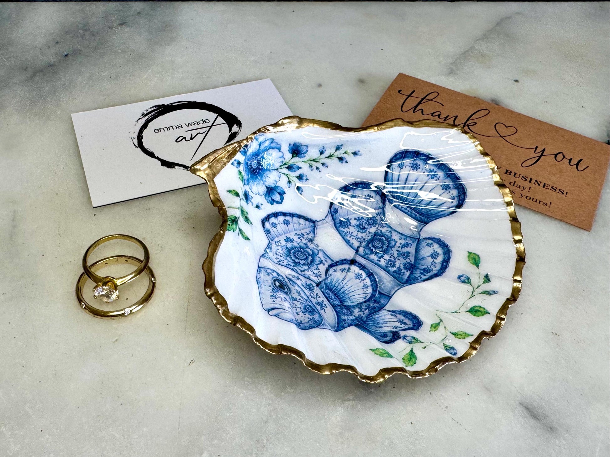Clownfish scallop shell trinket dish featuring an original illustrated Delft Blue design by Emma Wade ART. Natural scallop shell finished with gold leaf or silver leaf edging and a crystal-clear glossy resin coating. Coastal jewellery tray, ring holder and ocean-inspired gift for fish and sea lovers, beach house décor, weddings, bridesmaids and nautical homes.