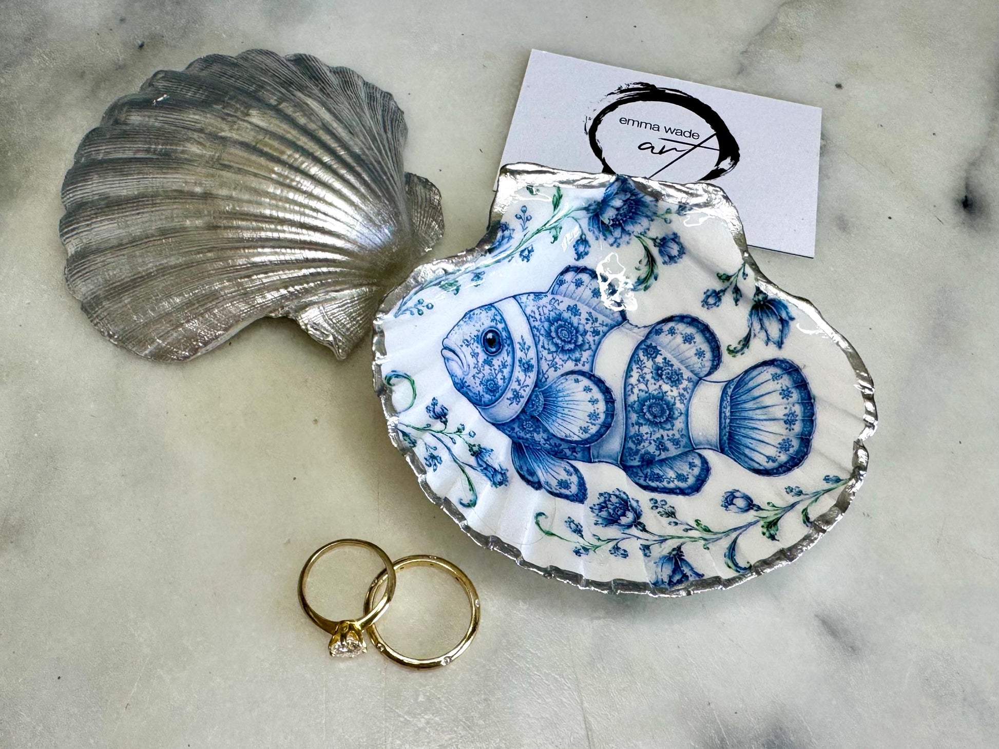 Clownfish scallop shell trinket dish featuring an original illustrated Delft Blue design by Emma Wade ART. Natural scallop shell finished with gold leaf or silver leaf edging and a crystal-clear glossy resin coating. Coastal jewellery tray, ring holder and ocean-inspired gift for fish and sea lovers, beach house décor, weddings, bridesmaids and nautical homes.